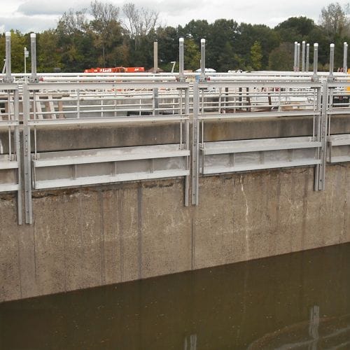 Multiple dual stem aluminum sluice gates installed on the sides of a concrete wall.