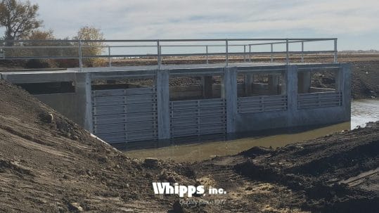 Concrete flood control gates installed in a water management system with muddy surroundings and visible railings.