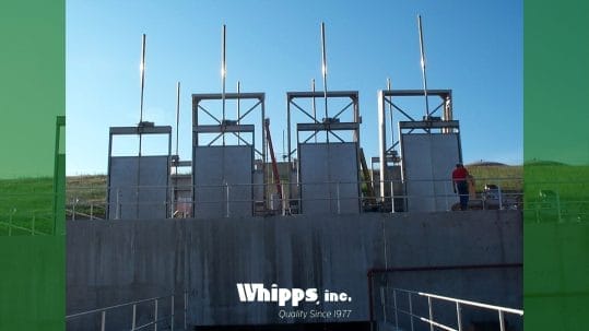 Four large embedded slide gates installed in a concrete water control structure, with vertical operating stems and a worker nearby for scale.