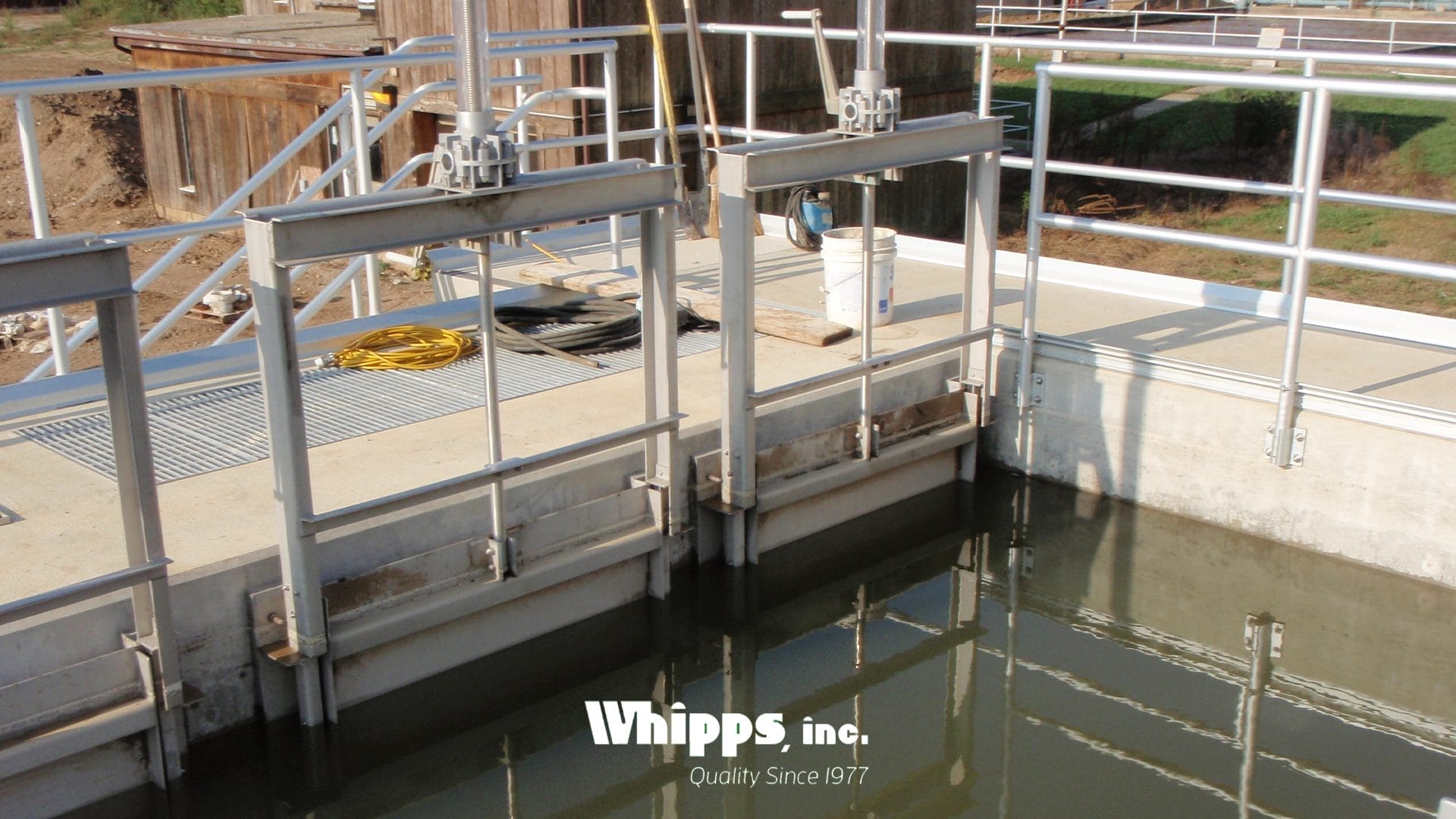 Slide gates installed side-by-side in an open concrete basin at a wastewater treatment plant, controlling foam-laden effluent.