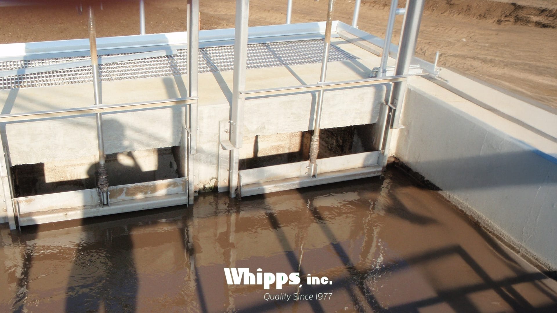 Slide gates installed side-by-side in an open concrete basin at a wastewater treatment plant, controlling foam-laden effluent.