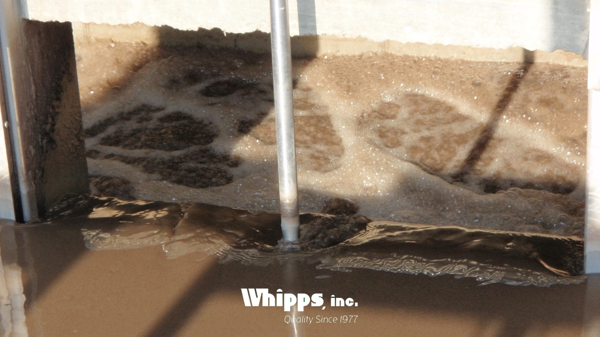 A close-up view of an open stainless steel slide gate in an active wastewater channel, with visible surface turbulence and debris.